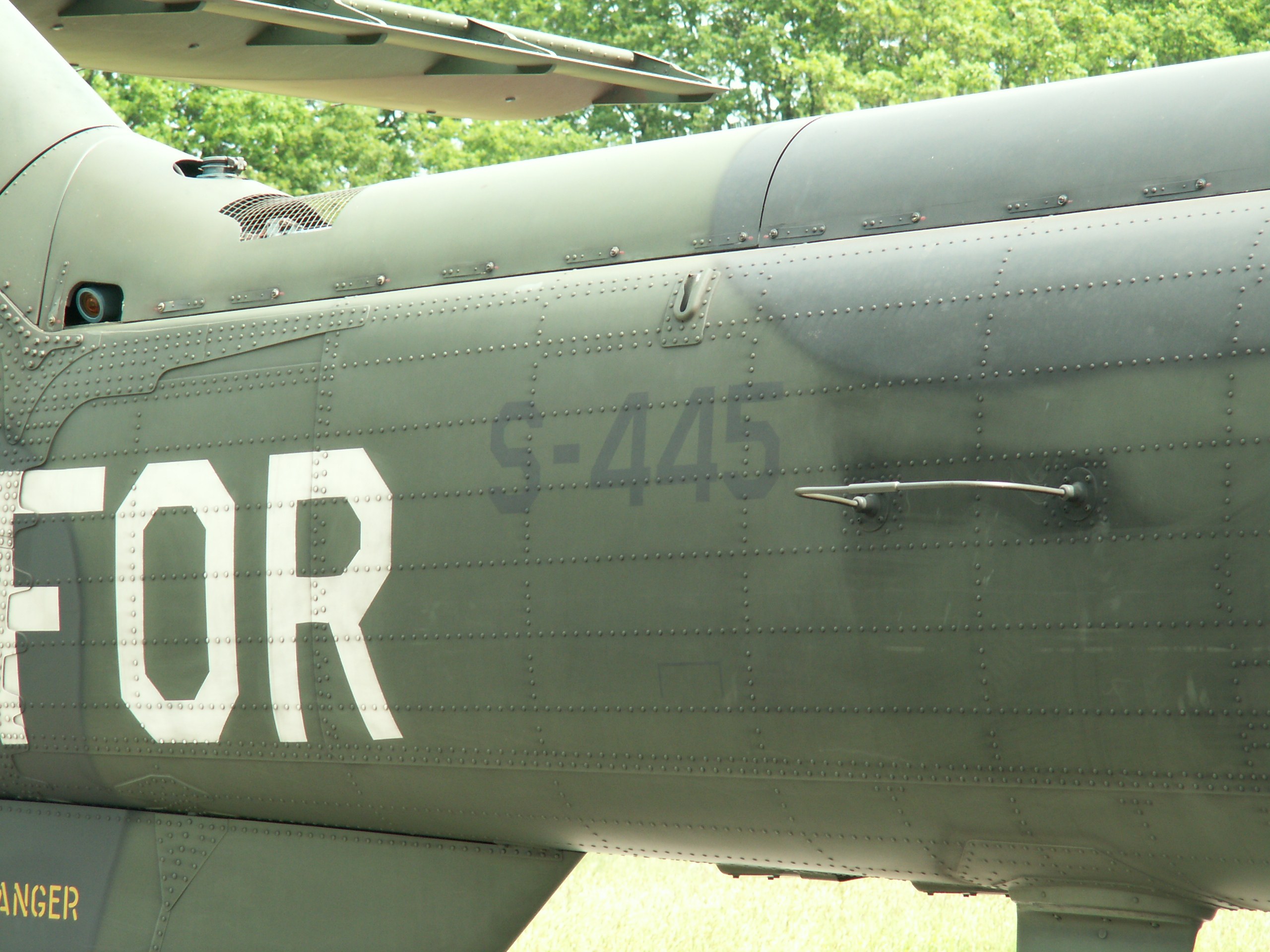 Nahaufnahme eines Militärhubschraubers mit der Aufschrift "FOR" an der Seite, vor einem Waldhintergrund.