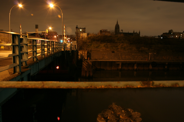 Eine Brücke spannt einen Fluss mit zahlreichen Straßenlaternen und im Hintergrund sind Gebäude zu sehen.