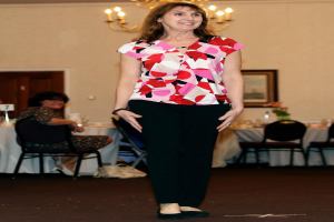 Eine Frau, die vor einem Bild an der Wand steht und lächelt, mit einer anderen Frau, die auf einem Stuhl neben einem Tisch mit einer Vase sitzt.