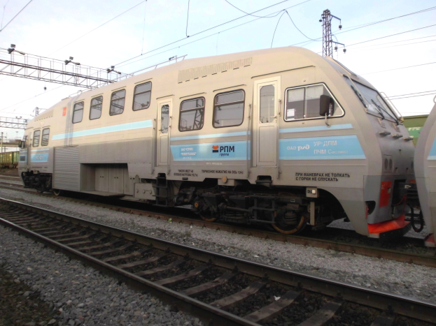Ein diesel-elektrischer Lokomotive fährt auf Schienen neben einem anderen Zug, mit Strommasten und Kabeln im Hintergrund unter einem klaren blauen Himmel.