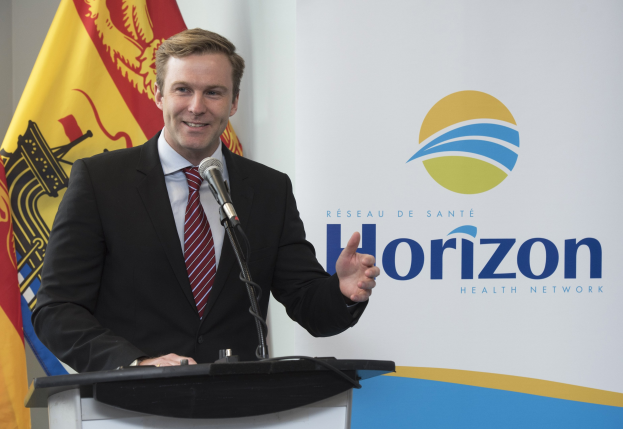 Ein Mann in einem schwarzen Blazer, weißem Hemd und roter Krawatte steht an einem Podium mit einem Mikrofon und einem Banner im Hintergrund und spricht als Chief Executive Officer.