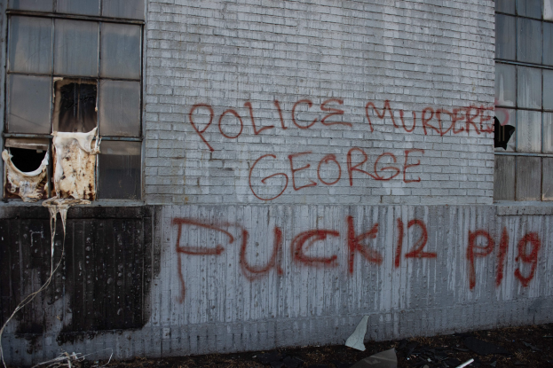 Graffiti an einer Gebäudewand mit der Aufschrift "Polizeimord George Fuck 12 P19" und Fenstern und verstreuten Gegenständen davor.