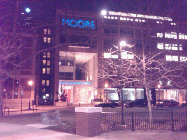 Ein Krankenhausgebäude mit Fahrzeugen davor, umgeben von Bäumen und einem Zaun.