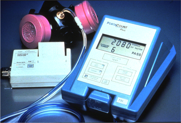 Eine Gasmaske auf einem Tisch neben einem elektronischen Gasdetektionsgerät mit einem angeschlossenen Kabel.