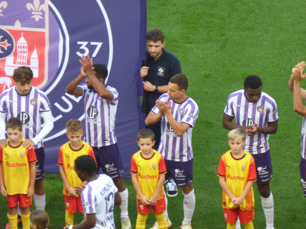 Eine Gruppe junger Jungs auf einem Fußballfeld, die klatschen, mit einem Banner und Logos im Hintergrund auf grünem Gras.