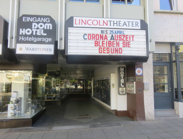 Außenansicht des Lincoln Theaters in Berlin, Deutschland, mit Glasfenstern und -türen sowie einer Schautafel und einem Inneren, das eine belebte Stadtkulisse suggeriert.