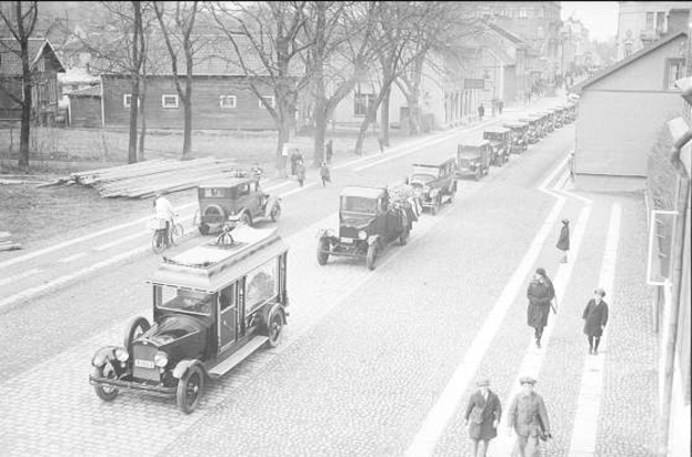 Ein Schwarz-Weiß-Foto einer Berliner Straße aus den 1930er bis 1940er Jahren mit Autos, Passanten, Gebäuden, Bäumen und einem klaren Himmel.
