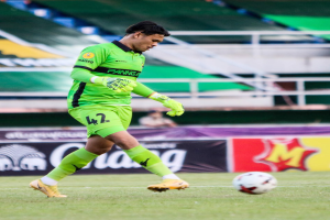Ein Mann in einem grünen Torwarttrikot schießt einen Fußball auf einem Rasenfeld in einem Stadion, im Hintergrund sind Banner mit der Aufschrift "Chivas USA gegen Mexico City, 3:1, Copa Libertadores".