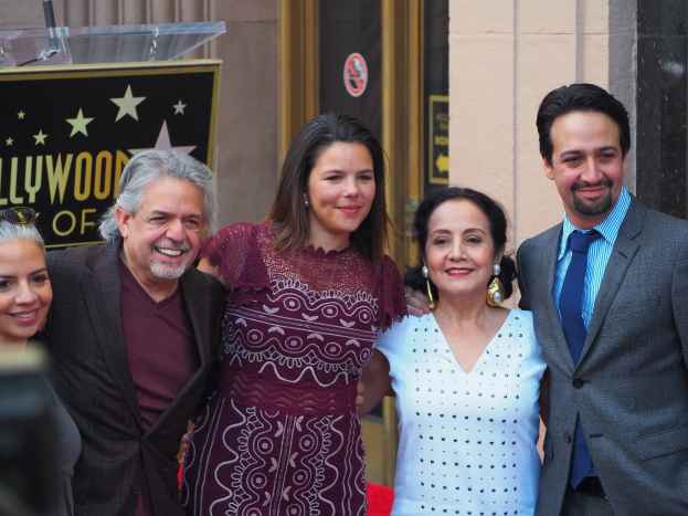 Gruppe von Menschen, die auf einer roten Teppich bei der Zeremonie des Hollywood Walk of Fame posen, mit einer Tafel, einem Glaspodium und einer Wand im Hintergrund.