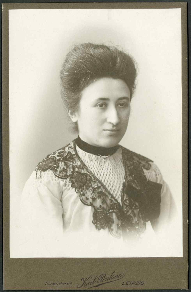 Schwarz-weißes Porträt einer Frau in einem weißen Kleid mit einem gemusterten Schultertuch, identifiziert als Karl Pinkau Leipzig, die direkt in die Kamera schaut.