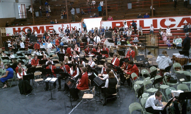 Eine Gruppe von Kindern sitzt auf Stühlen in einem Stadion für eine Musikstunde, mit leeren Stadionplätzen im Hintergrund.