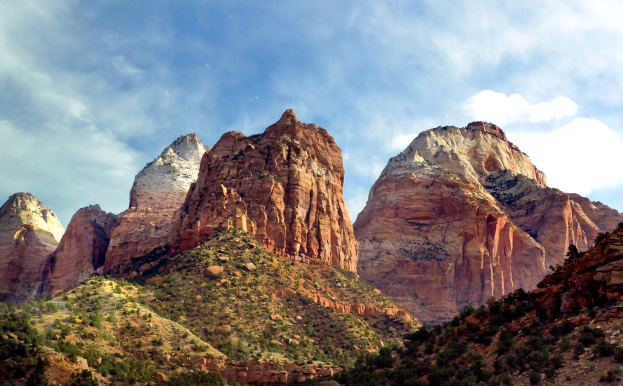 Eine malerische Aussicht auf den Zion-Nationalpark in Utah mit majestätischen Bergen, grünen Bäumen, steinigem Gelände und einem Himmel mit weißen Wolken.