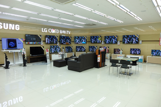 Ein geräumiger Raum mit mehreren an den Wänden montierten Fernsehern, umgeben von Sofas, Tischen, Stühlen und anderen Möbeln, beleuchtet von Deckenlampen.