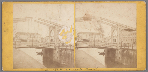 Ein altes Foto einer Brücke unter Reparaturarbeiten, die über ein Gewässer führt, mit verstreuten Werkzeugen und Materialien und Gebäuden im Hintergrund.