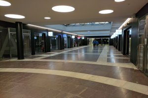 Ein langer Flur mit Menschen, die von Deckenlampen beleuchtet werden, umgeben von Säulen und Glastüren, mit Texttafeln, die den Eindruck einer belebten Stadtverwaltung vermitteln.