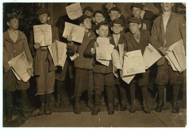 Schwarzes und weißes Foto einer Gruppe junger Jungs, die zusammenstehen und jeweils eine Zeitung halten.