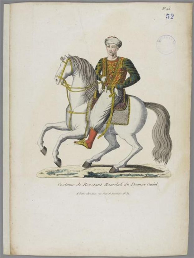 Ein Mann in einem farbenfrohen, detailreichen Kostüm eines Manelak aus dem Premierhof reitet auf einem weißen Pferd, das mit Sattel und Zaumzeug geschmückt ist.