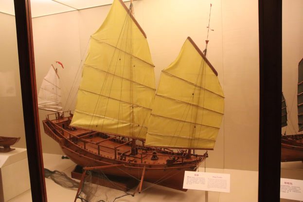 Ein hölzernes Modellsegelboot in einer Glasvitrine mit informativen Schautafeln an den umliegenden Wänden.
