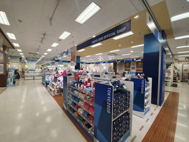 Das Innere eines offiziellen Tokyo 2020-Shops mit Kleiderstangen, Namensschildern, Deckenlampen und verschiedenen anderen Gegenständen.