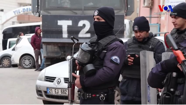 Eine Gruppe von Polizisten in Uniformen mit Waffen auf einer Straße in Ankara, Türkei, während einer Anti-Regierungsdemo, mit Fahrzeugen, Menschen, Gebäuden und Texttafeln im Hintergrund.