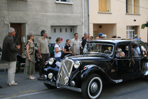 Ein Auto fährt auf einer Straße mit Menschen und Gebäuden auf der linken Seite.