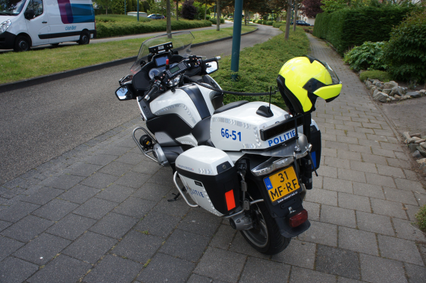 Ein Polizeimotorrad am Straßenrand mit einem Helm darauf, umgeben von Bäumen, Polen, Gebäuden und anderen Fahrzeugen.