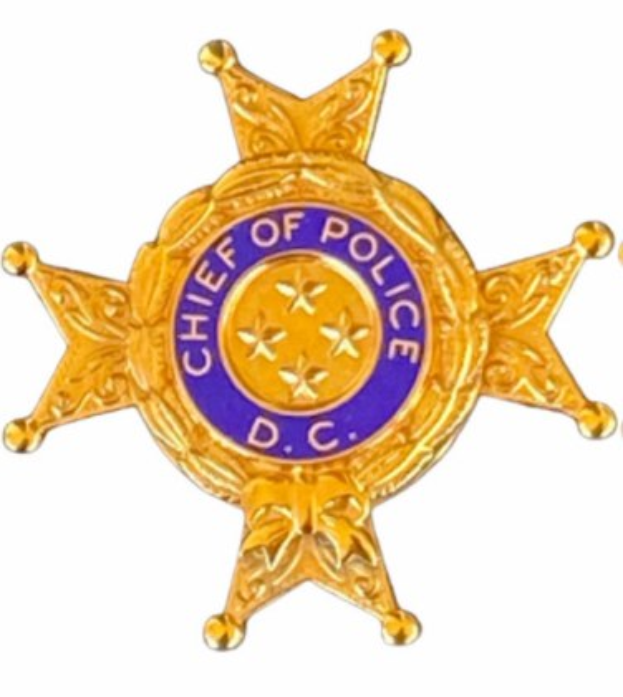 Polizeibeamte in Uniform vor einem Glasgebäude mit einer Stange links und Schildern mit 'Friedrichshain Kreuzberg' Text im Hintergrund.