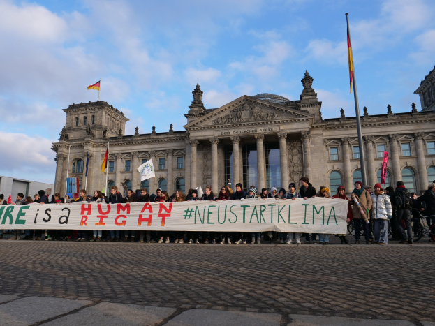 Eine Gruppe von Menschen steht vor dem Reichstaggebäude in Berlin und hält ein Banner mit der Aufschrift "Wir sind ein Menschenrecht" in den Händen.