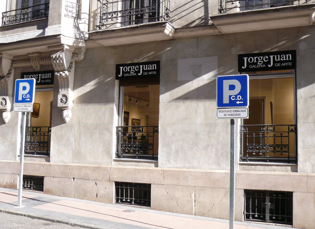 Ein mehrstöckiges Gebäude mit Fenstern, Geländern, Türen und Säulen, das Schilder an Pfählen entlang des Gehwegs und sichtbare Innenobjekte zeigt, die auf eine belebte städtische Umgebung hindeuten.