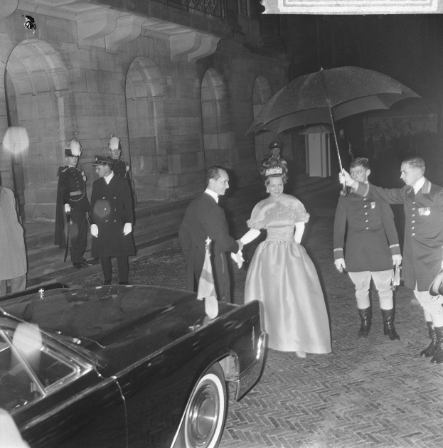 Schwarzes und weißes Foto von Queen Elizabeth II und Prinz Philip, Duke of Edinburgh, bei der Ankunft in Buckingham Palace; sie hält einen Blumenstrauß, er trägt einen Regenschirm, beide in formeller Kleidung vor einem Hintergrund ausbogiger Architektur.