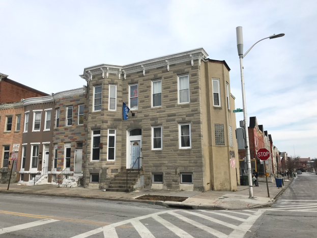 Eine Reihe neuer Häuser an einer Straßenecke in Philadelphia, mit Fenstern, Türen, Treppen mit Geländern, Laternen, Schildern und Fahrzeugen auf der Straße, mit Bäumen und einem bewölkten Himmel im Hintergrund.