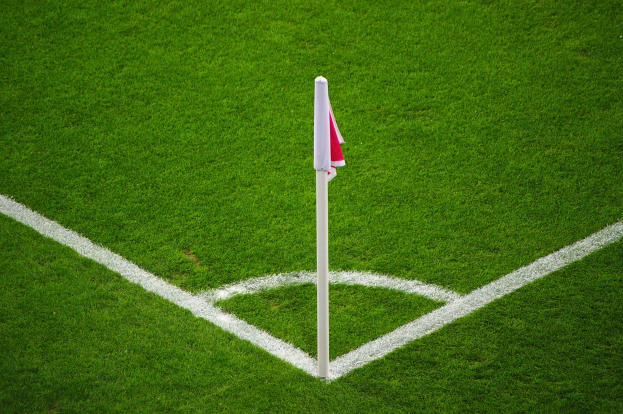 Ein Fußballfeld mit grünem Rasen, weißen Begrenzungslinien und einem weißen Pfosten mit einer roten und weißen Flagge auf dem Elfmeterpunkt.