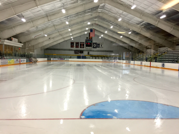 Großes Hallen-Eisstadion mit Deckenbeleuchtung, Werbetafeln, einer Wand im Hintergrund, Treppen mit Geländern und einigen Menschen, was auf eine Sportanlage hinweist, die likely für Hockey genutzt wird.