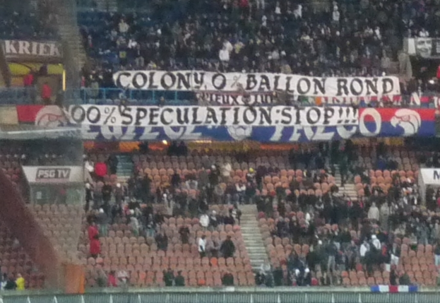 Ein Stadion voller Menschen, Banner und Stühle, mit einem Zaun unten und Treppen links.