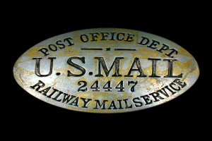 Ein ovalförmiges Metallobjekt mit der Aufschrift "Post Office Dept. U.S. Mail 2447 Railway Mail Service" auf einem schwarzen Hintergrund.