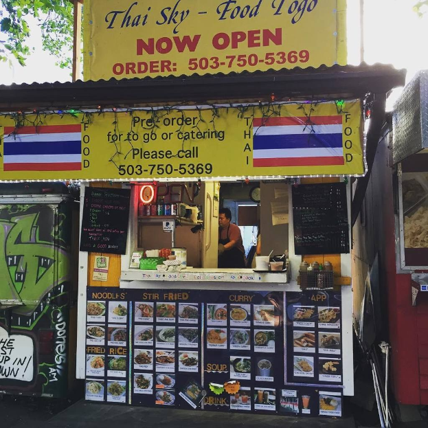 Läden, Getränkedosen, Speisekarten, eine Uhr, Gewürze in Plastikbehältern, Gewürze, Werbetafeln, Namensschilder und der Himmel.