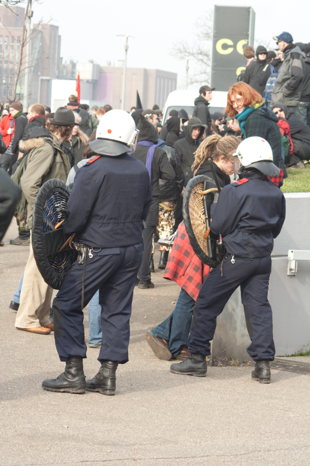 Eine Gruppe von Menschen, die auf einer Straße gehen, mit zwei Personen in der Vornahme, die wie Polizei aussehen, Gebäude im Hintergrund und Boden unten.