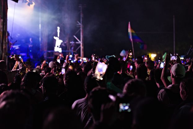 Eine Menge bei einem Konzert hält leuchtende Handys hoch, während Musiker auf der Bühne spielen.