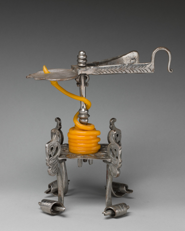 Ein metallener Korkenzieher mit einer hellgelben Feder oben drauf, mit einem zylindrischen Körper, einem Griff auf einer Seite und einem Ausguss auf der anderen.