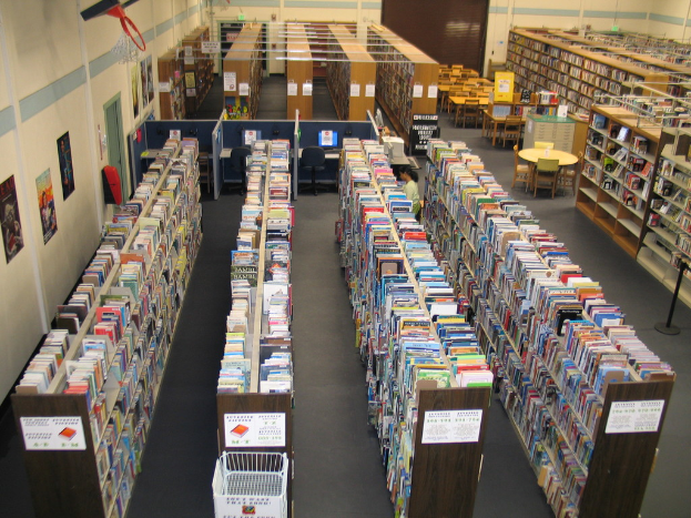 Eine Bibliothek mit Bücherregalen, Tischen und Stühlen vor einer Wand.