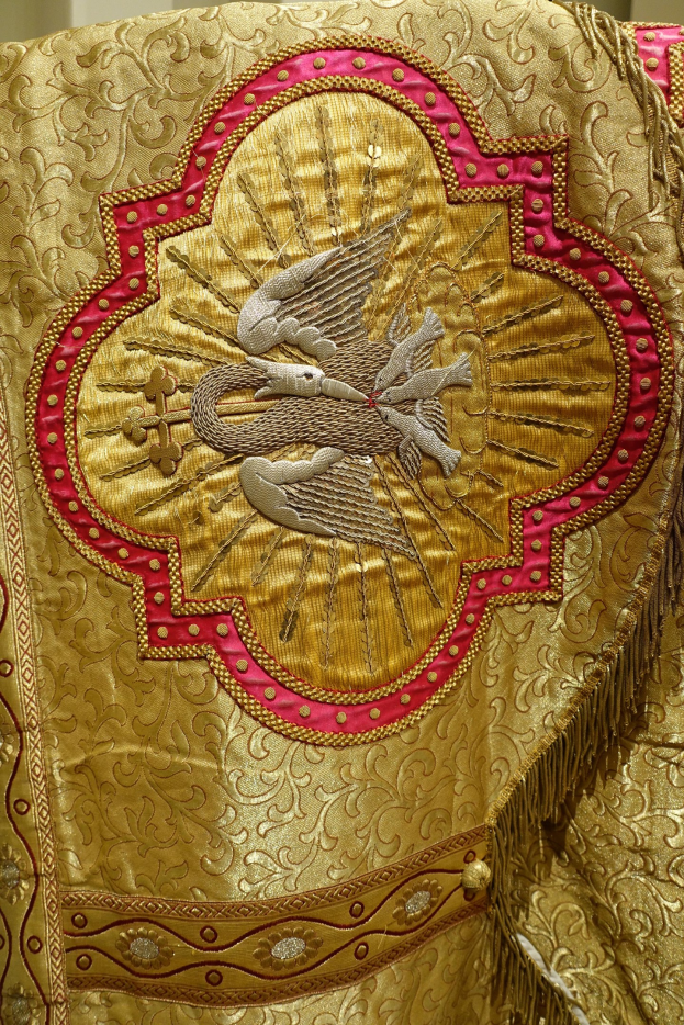 Nahaufnahme eines Priestergewandes mit goldenen und roten Stickereien an einer Wand im Hintergrund.