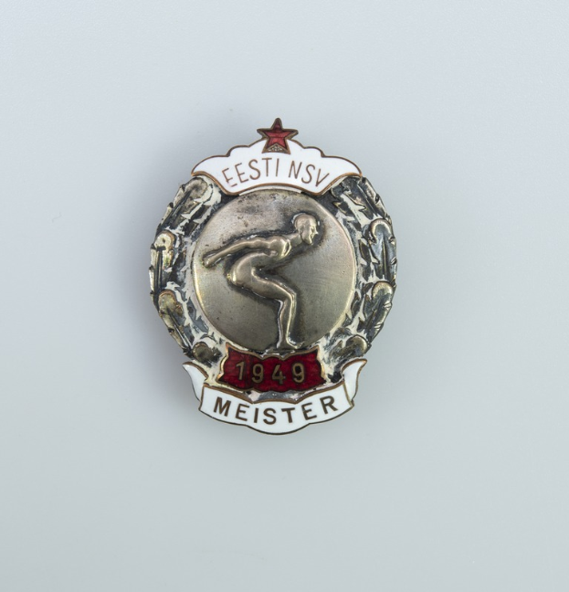 Ein silbernes Abzeichen mit einem roten Stern, Emblem der Olympischen Spiele 1949 in Deutschland, mit Text in der Mitte des Bildes.