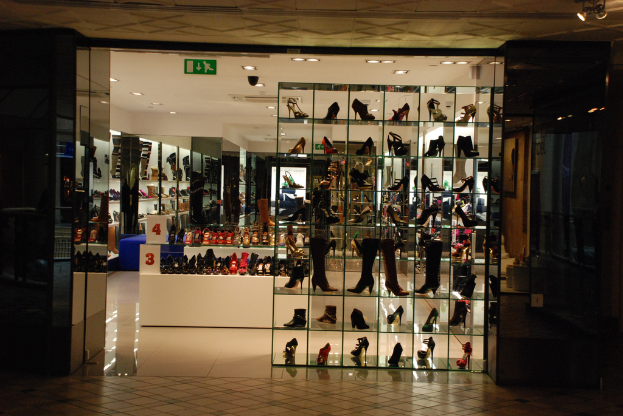 Eine Schuhgeschäftsauslage mit verschiedenen Schuhen und Sandalen auf einem weißen Tisch, mit einer Wand auf der linken Seite und einer Decke oben.