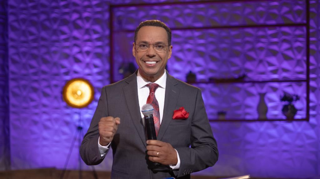 Stephen Colbert, Moderator von 'The Daily Show with Trevor Noah', steht auf einer Bühne und hält ein Mikrofon, trägt einen Anzug, Krawatte und Brille, mit einem Scheinwerfer und Ständer hinter ihm.