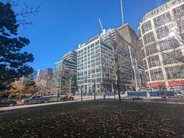 Eine Straße in Toronto mit hohen Geböuden, Fahrzeugen, Füpfaden, Böumen und trockenen Blüttern auf dem Boden unter einem sichtbaren Himmel.