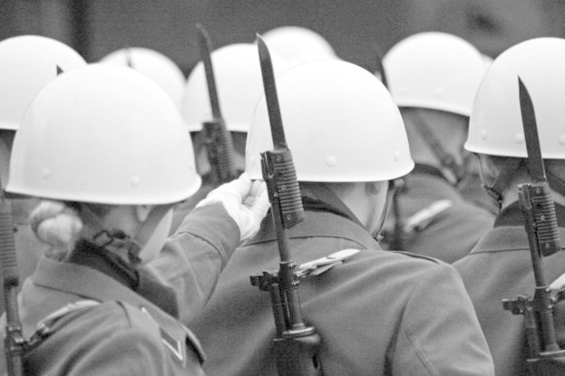 Ein Schwarz-Weiß-Bild von mehreren uniformierten Personen mit Hüten, die Waffen halten und vom Betrachter wegschauen.