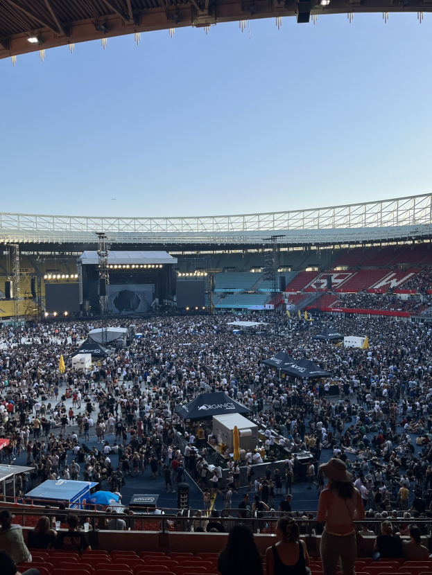Große Menschenmenge auf Sitzplätzen und Stehplätzen in einem Stadion mit Zelten, Geländern und Überdachung, vor einem Himmel als Hintergrund am O2 Arena in London.