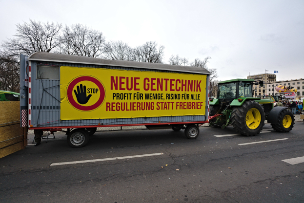 Ein Lastwagen mit einer Tafel fährt während einer Demonstration in Deutschland eine Straße entlang, umgeben von Menschen, Bäumen, Gebäuden und einem klaren blauen Himmel.