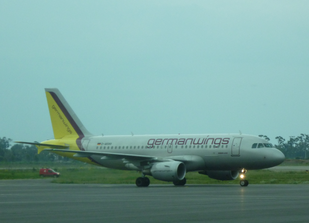 Ein Airbus A320-200 der Germanwings auf dem Rollfeld des Frankfurter Flughafens mit einem Fahrzeug auf der linken Seite, Gras, Bäumen und dem Himmel im Hintergrund.