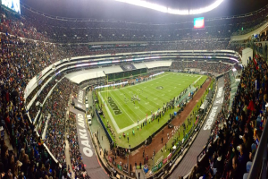 Ein großes Stadion mit Zuschauern, die ein Fußballspiel verfolgen, mit Spielern und verschiedenen Gegenständen auf dem Feld, beleuchteten Tafeln, Geländern, Bildschirmen und Deckenlampen.